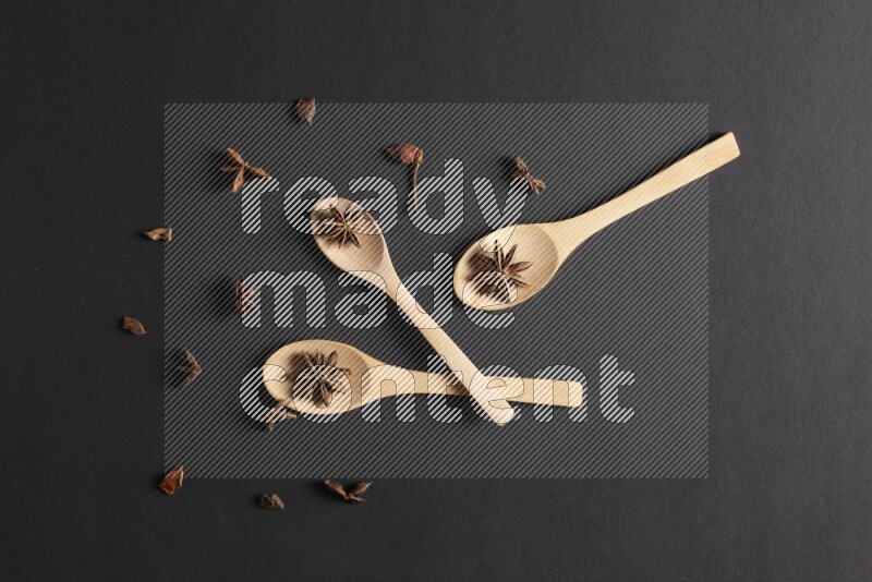 Star Anise in wooden spoons on black flooring
