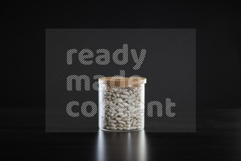 White beans in a glass jar on black background
