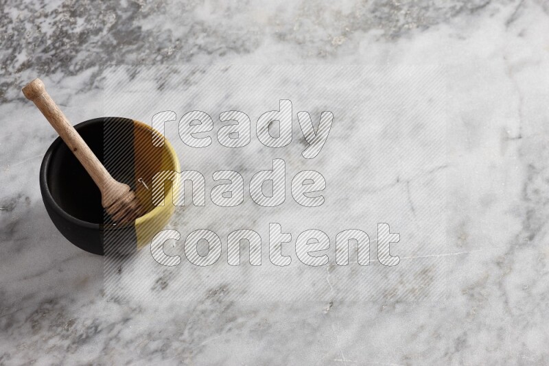 وعاء فخاري متعدد الألوان مع ملعقة عسل خشبية بداخله على خلفية من الرخام الرمادي