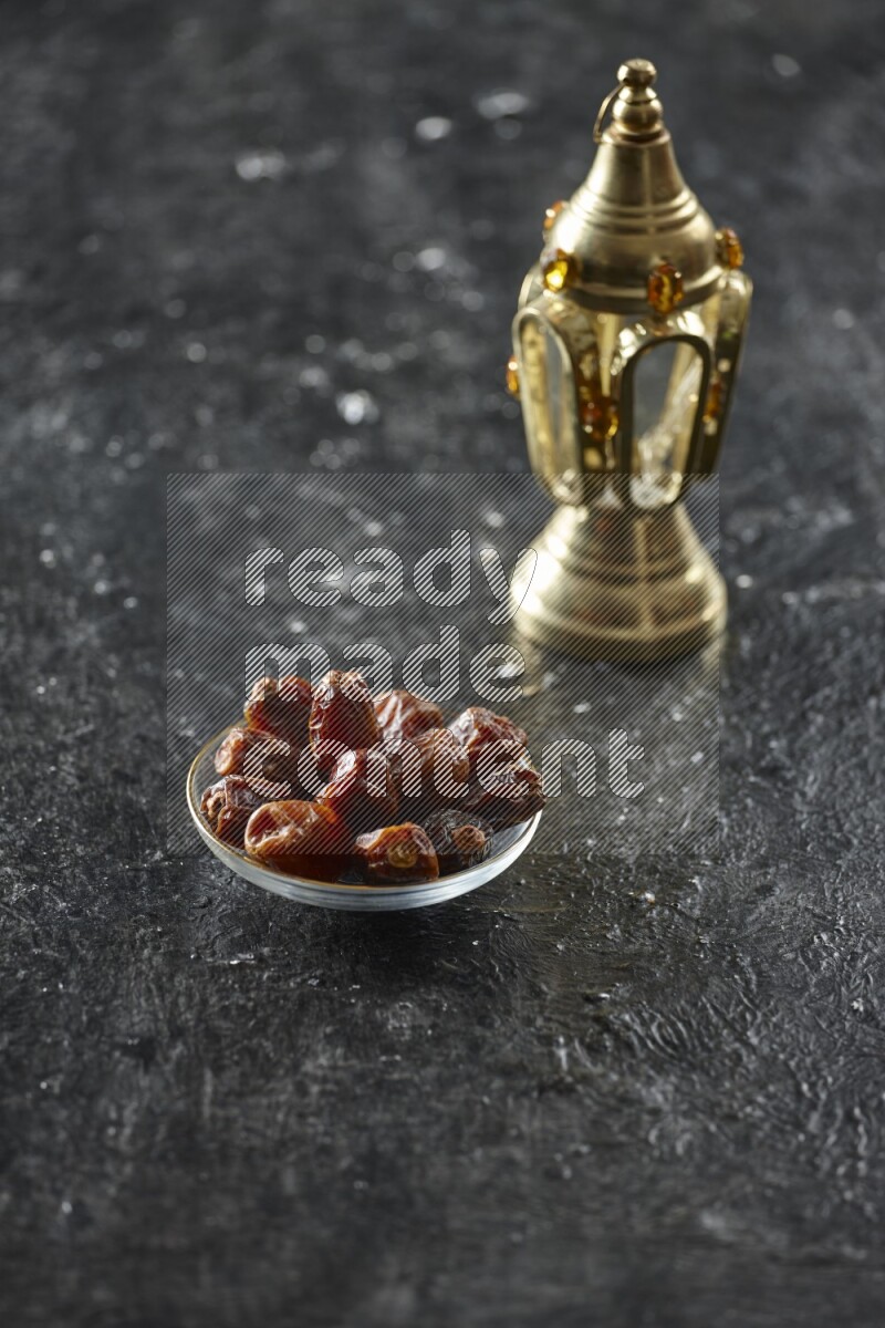 A golden lantern with different drinks, dates, nuts, prayer beads and quran on textured black background