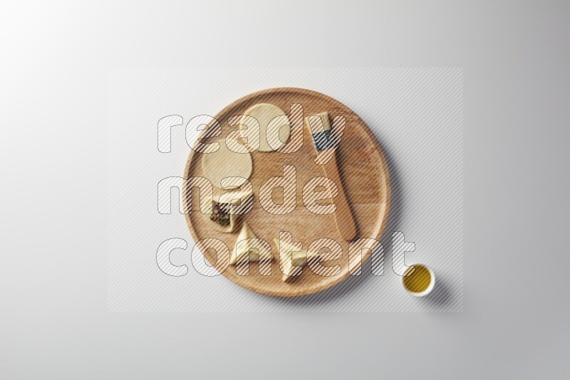 two closed sambosas and one open sambosa filled with meat while oil with oil brush aside in a wooden dish on a white background