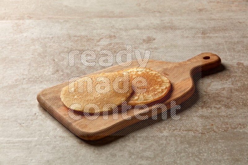 Two stacked plain pancakes on a wooden board on beige background