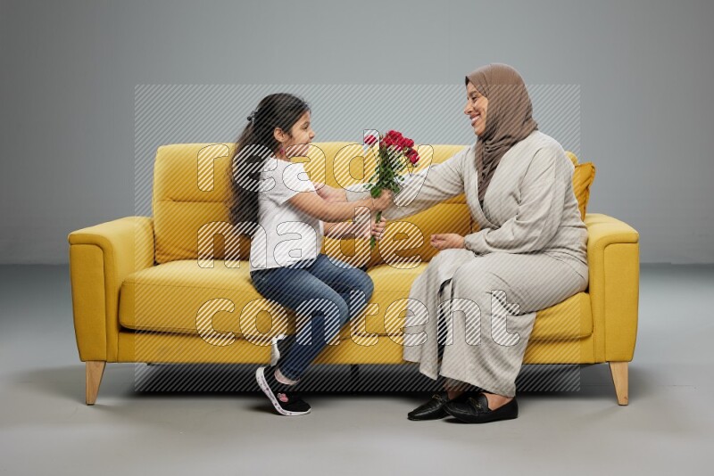 A girl sitting giving flowers to her mother on gray background