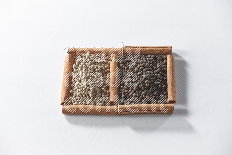 مربعان من أعواد القرفة ممتلئان بحبوب الفلفل الأسود والفلفل الأبيض علي خلفية بيضاء