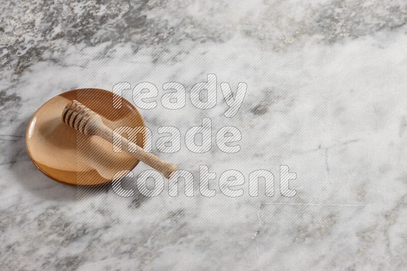 Multicolored pottery plate with wooden honey dipper in it on grey marble background