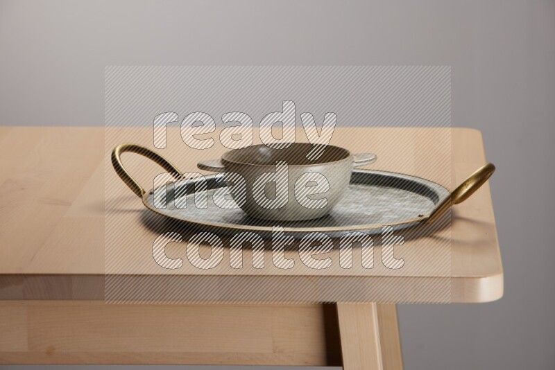 off white bowl placed on a rounded stainless steel tray with golden handels on the edge of wooden table