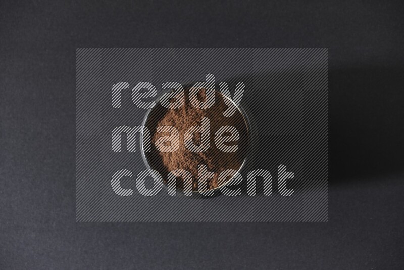 A black pottery bowl full of cloves powder on a black flooring