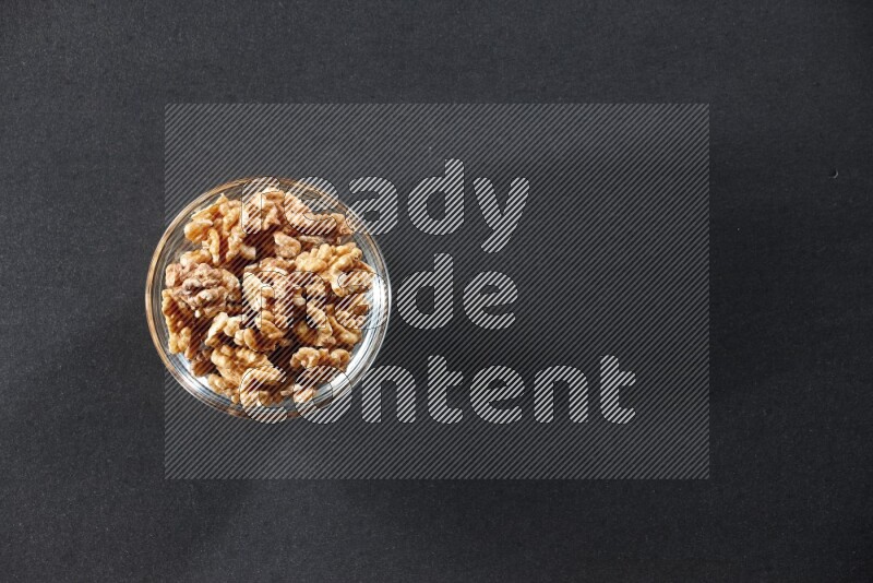 A glass bowl full of peeled walnuts on a black background in different angles