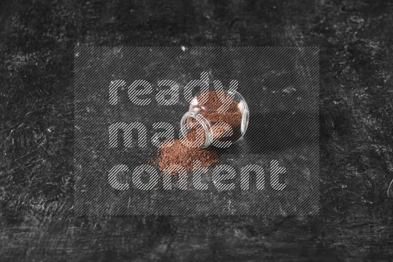 وعاء زجاجي مقلوب ممتلئ ببذور حب الرشاد وتناثرت البذور منه على أرضية سوداء