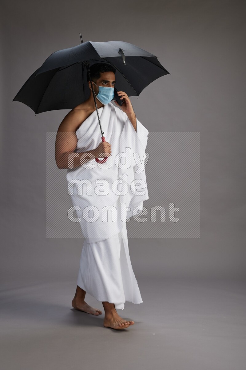 A man wearing Ehram and mask Standing holding umbrella on gray background on gray background