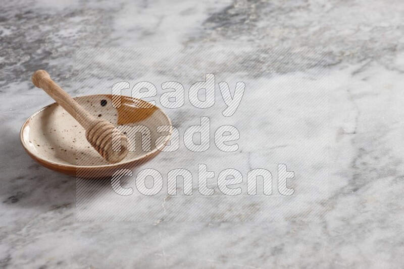Multicolored pottery plate with wooden honey dipper in it on grey marble background