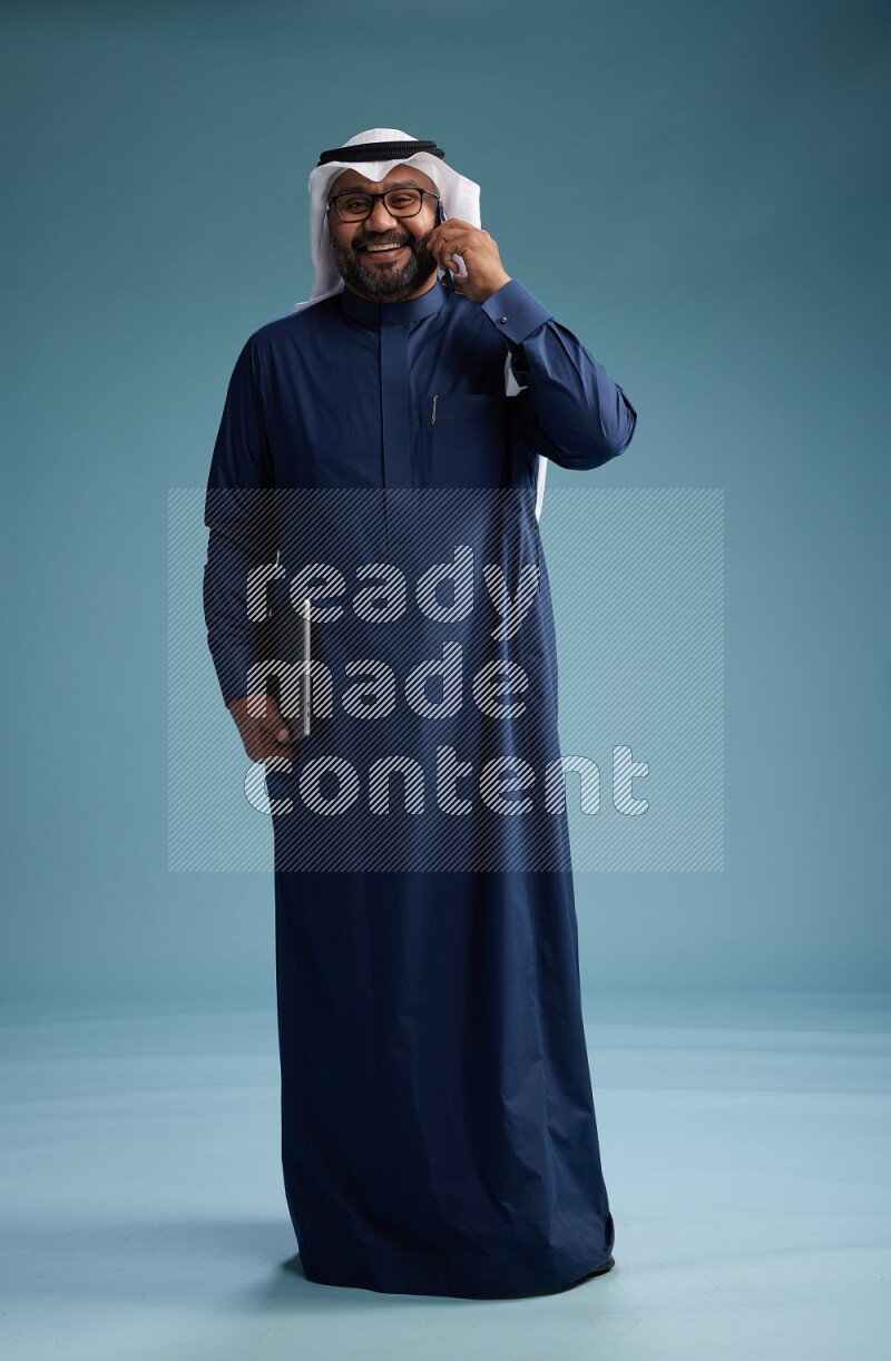 Saudi Man with shimag Standing talking on phone on blue background
