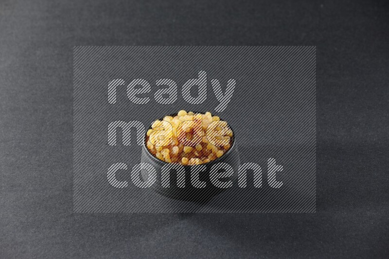 A black pottery bowl full of raisins on a black background in different angles