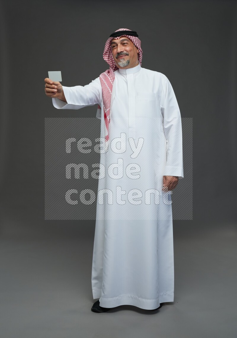 Saudi man with shomag Standing holding ATM card on gray background