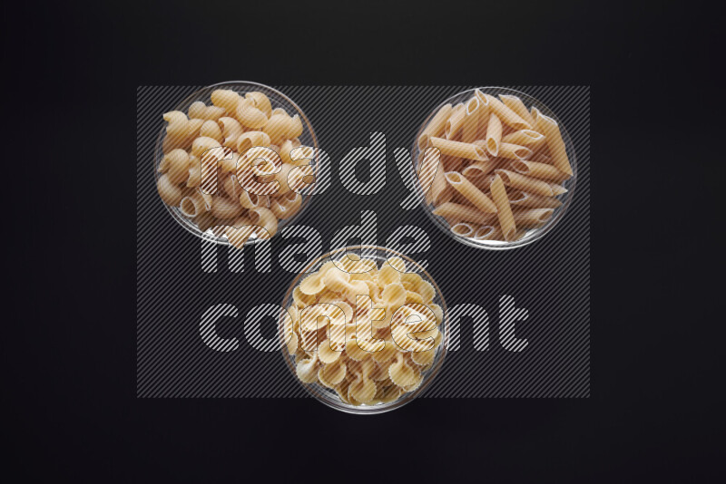 Different pasta types in glass bowls on black background