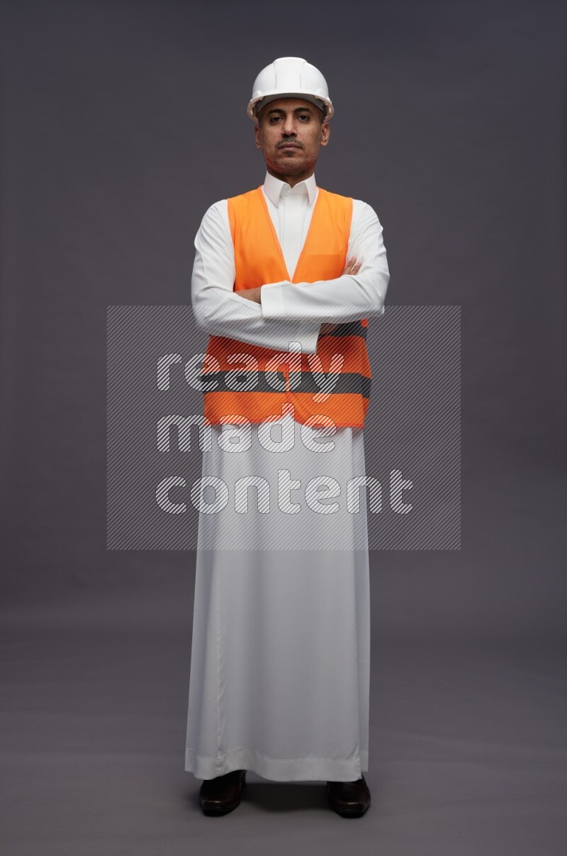 Saudi man wearing thob with engineer vest standing with crossed arms on gray background