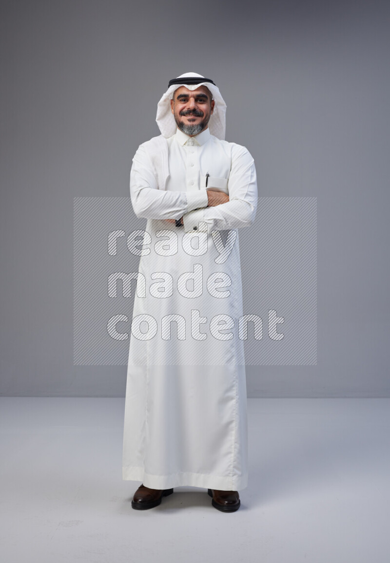 Saudi man Wearing Thob and white Shomag standing with crossed arms on Gray background