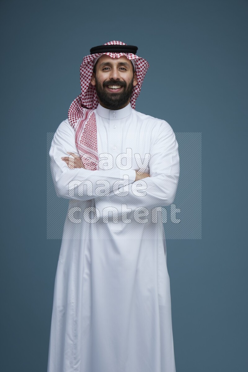 A man posing in a blue background wearing Saudi Thob and Shomag
