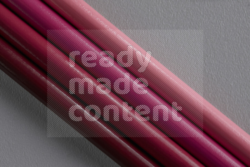 A collection of sharpened colored pencils arranged showcasing a gradient of pink hues on grey background