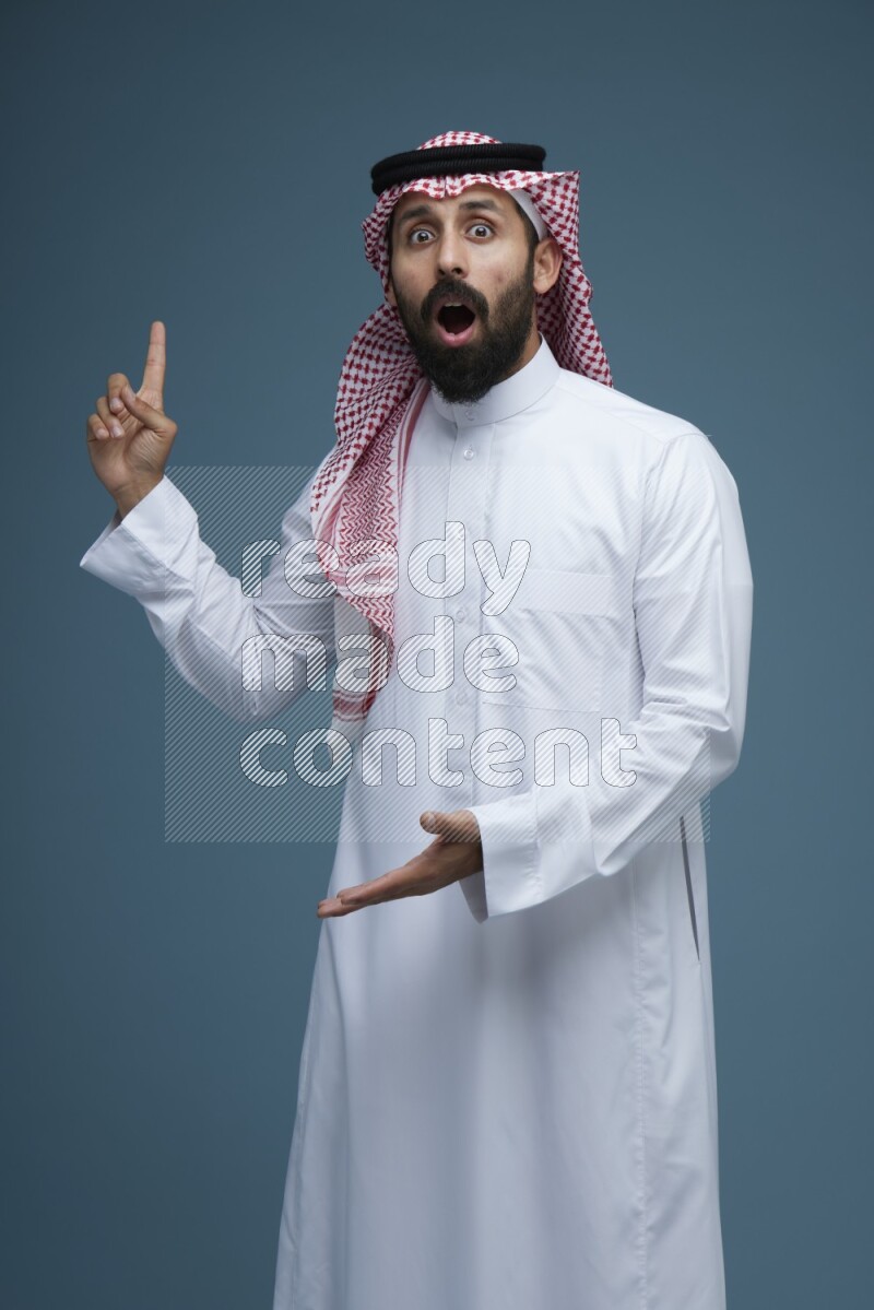 A man pointing in a blue background wearing Saudi Thob and Shomag