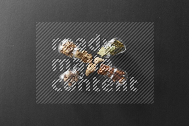 أوراق الغار وزنجبيل مجفف وقرفة وجوزة الطيب في أوعية زجاجية علي خلفية سوداء