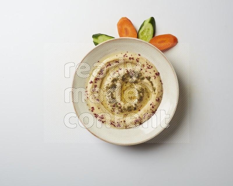 Hummus in a pottry plate garnished with zaatr & sumak on a white background