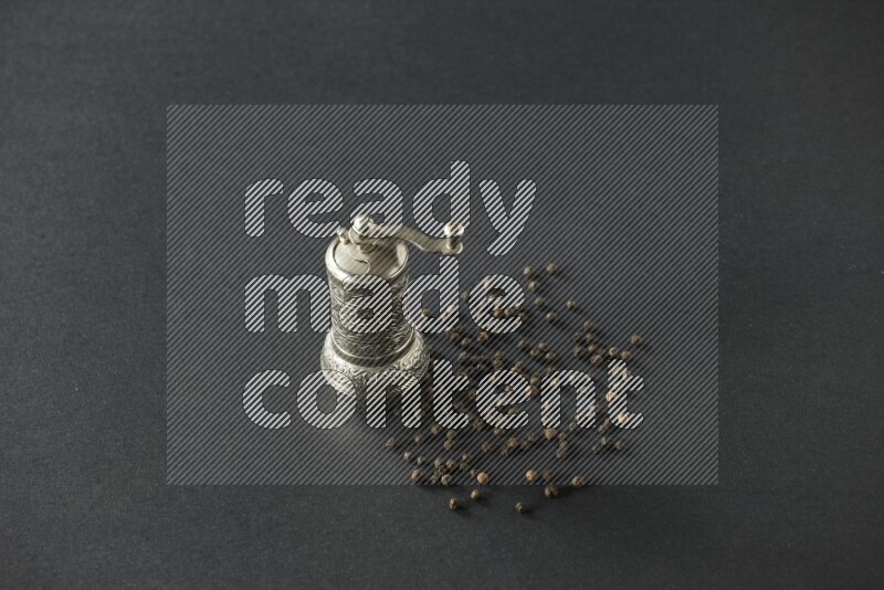 A turkish metal pepper grinder and spreaded black pepper beads on a black flooring