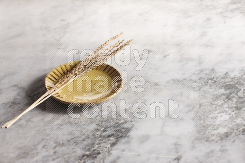 Wheat stalks on multicolored pottery plate on grey marble background