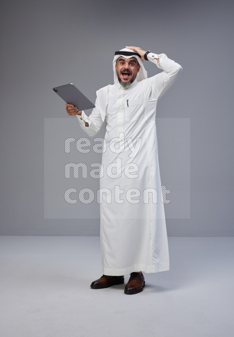 Saudi man Wearing Thob and white Shomag standing working on tablet on Gray background