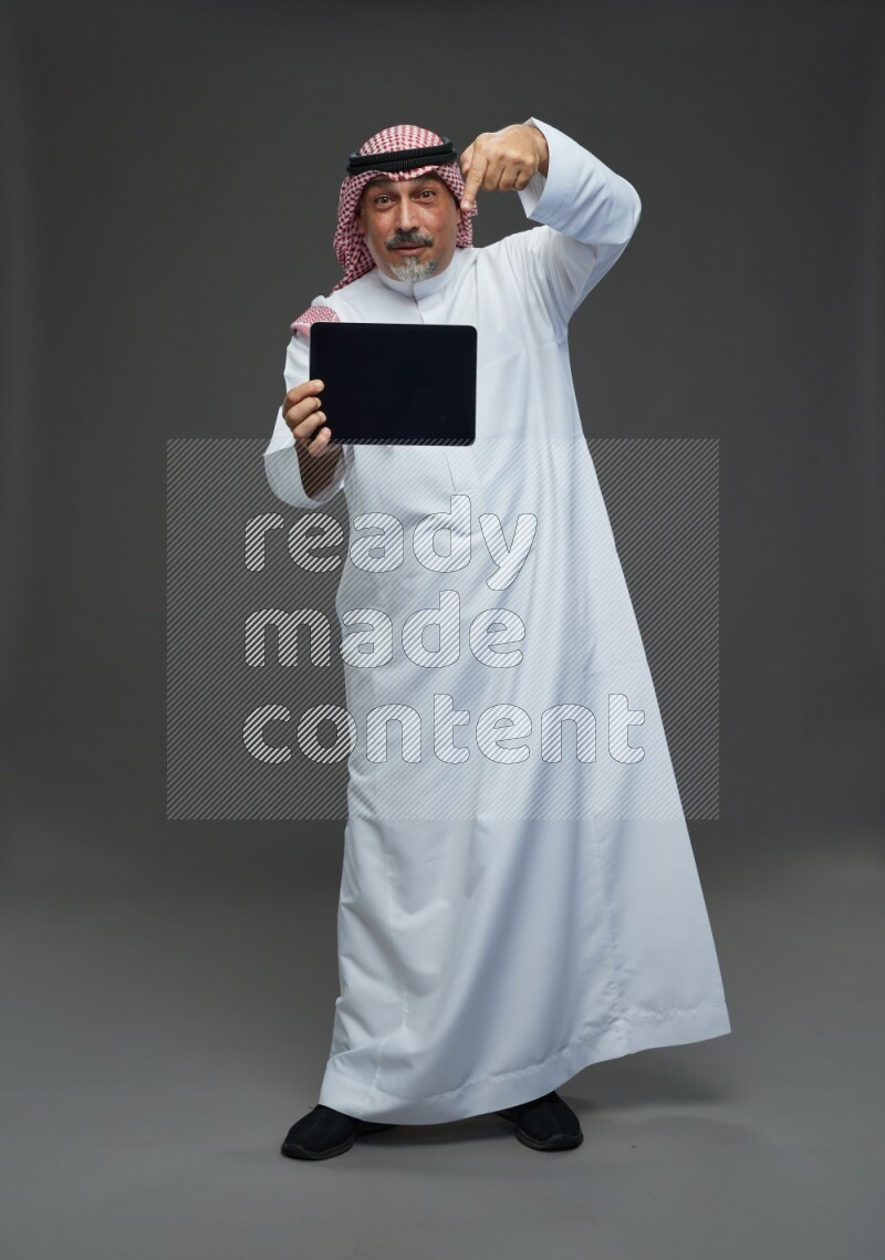 Saudi man with shomag Standing working on tablet on gray background