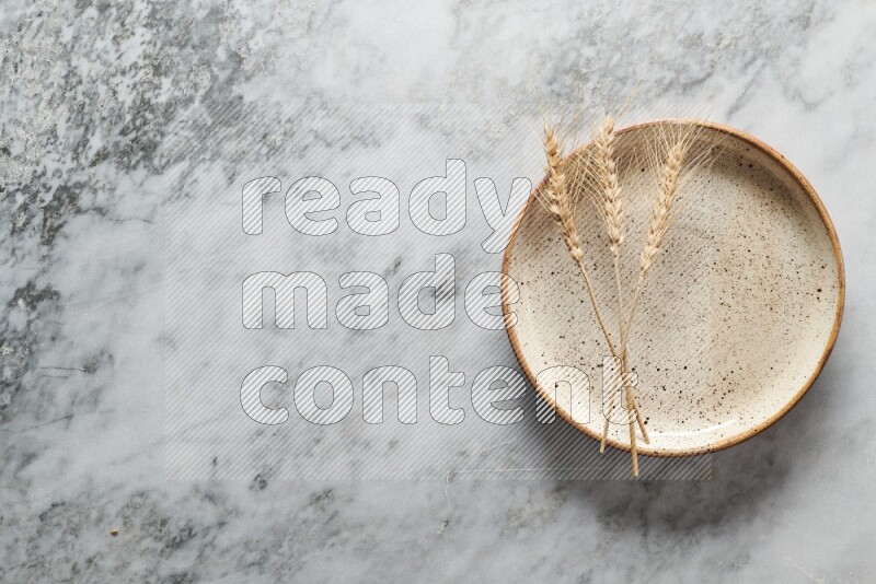 سنابل من القمح علي طبق فخاري متعدد الألوان علي خلفية من الرخام الرمادي