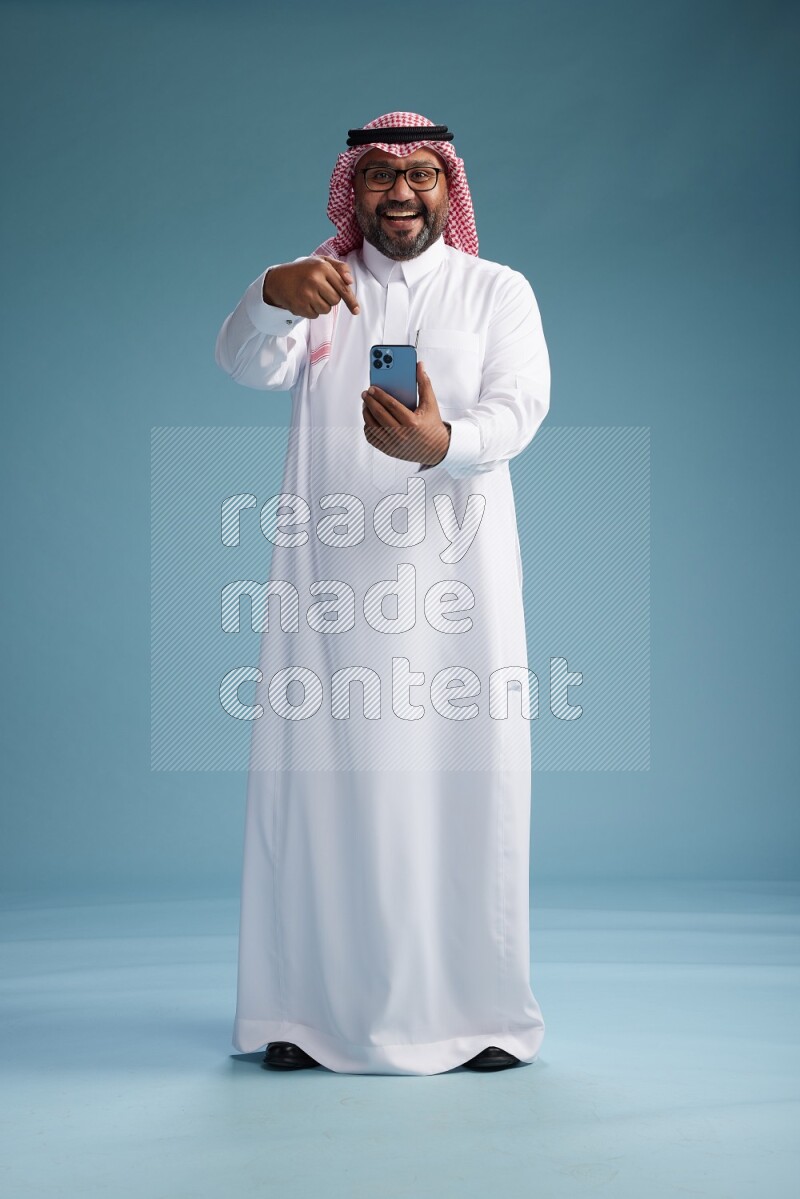 Saudi Man with shimag Standing texting on phone on blue background