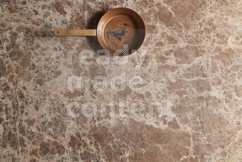 A small copper pan on beige marble background