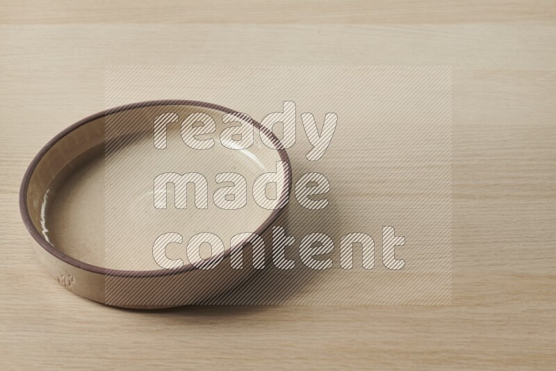 A beige pottery oven bowl on light wooden background