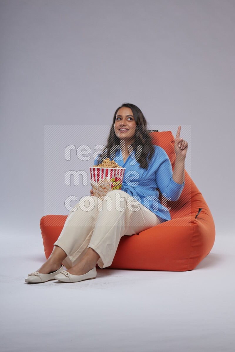 A woman sitting on an orange beanbag and eating popcorn