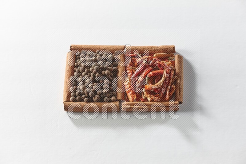 مربعان من أعواد القرفة ممتلئان بالفلفل الحار المجفف وحبوب بهار الفلفل الحلو علي خلفية بيضاء