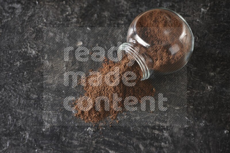 وعاء زجاجي للتوابل مقلوب ممتلئ ببودرة القرنفل والبودرة سقطت منه على أرضية سوداء