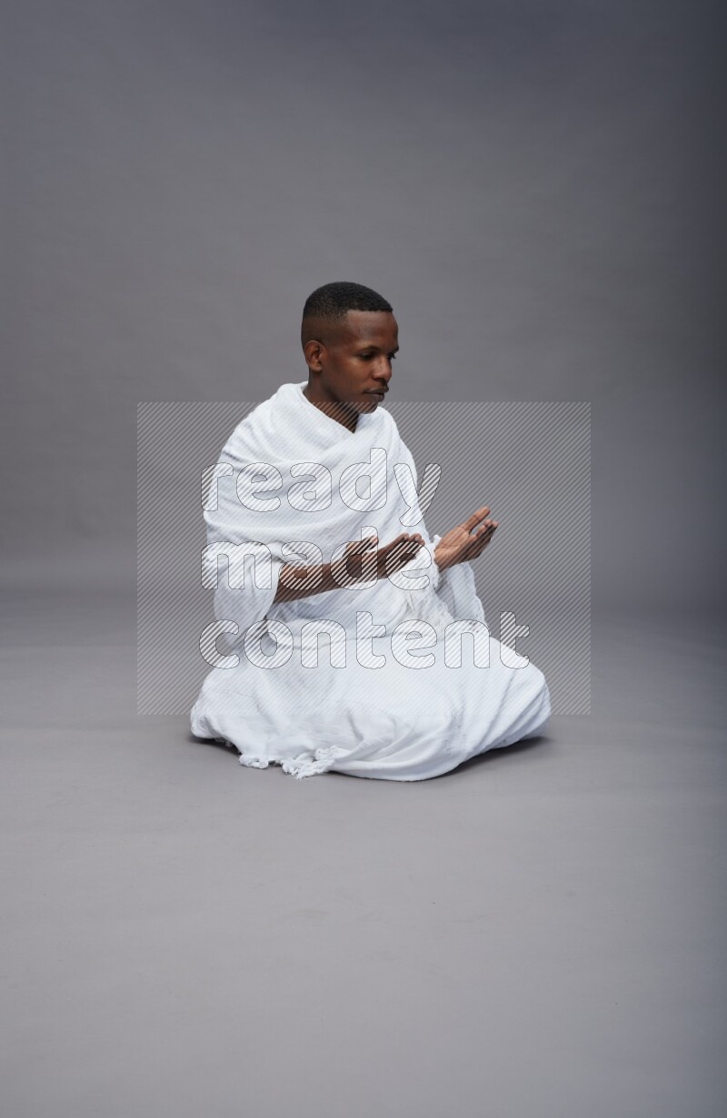 A man wearing Ehram sitting on floor dua'a on gray background
