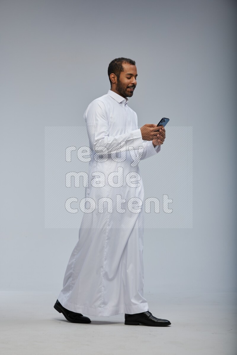 Saudi man wearing Thob standing texting on phone on Gray background
