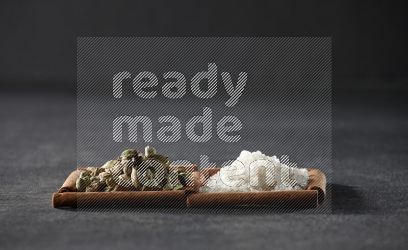 2 squares of cinnamon sticks full of white salt and cardamom on black flooring