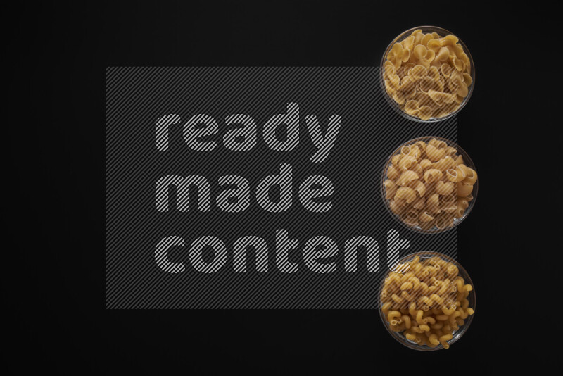 Different pasta types in 3 glass bowls on black background