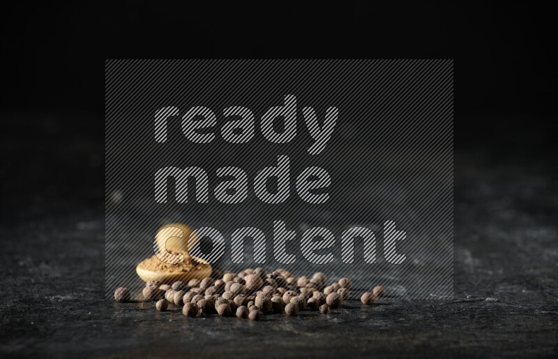 ملعقة خشبية ممتلئة ببودرة بهار الفلفل الحلو بجانب حبوب من الفلفل على خلفية سوداء