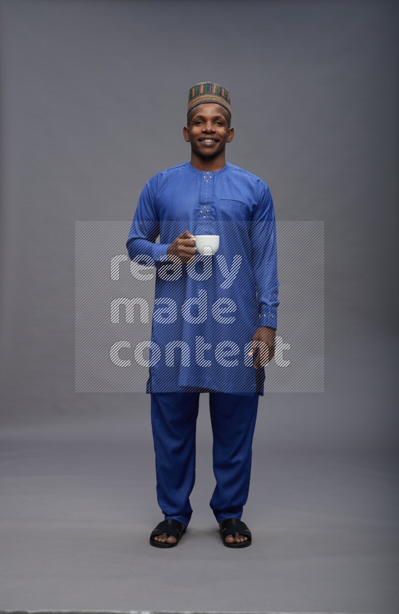 Man wearing Nigerian outfit standing holding mug on gray background