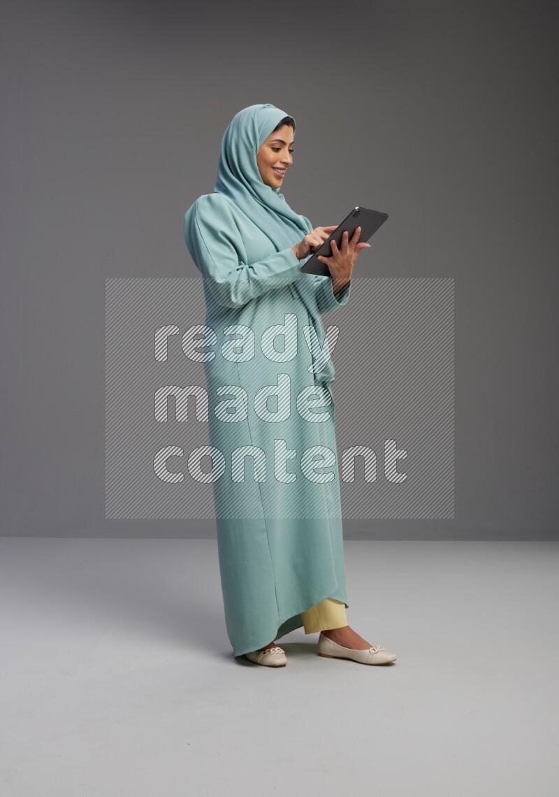Saudi Woman wearing Abaya standing working on tablet on Gray background