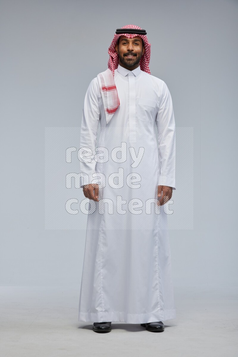 Saudi man Wearing Thob and shomag standing interacting with the camera on Gray background
