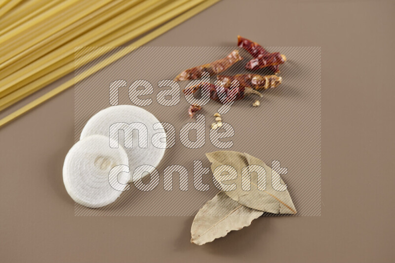 Raw pasta with different ingredients such as cherry tomatoes, garlic, onions, red chilis, black pepper, white pepper, bay laurel leaves, rosemary and cardamom on beige background