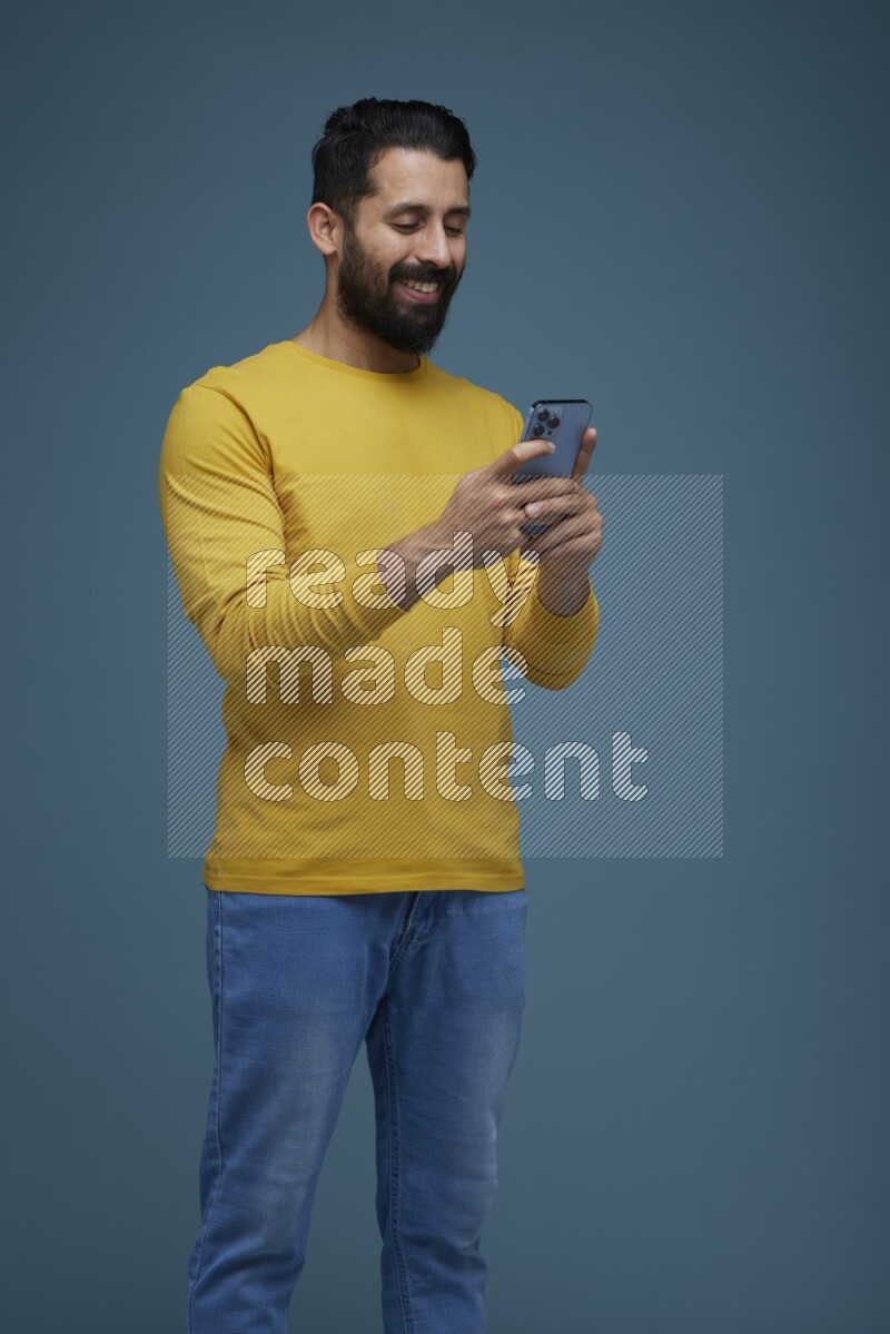 Man typing on his phone in a blue background wearing a yellow shirt