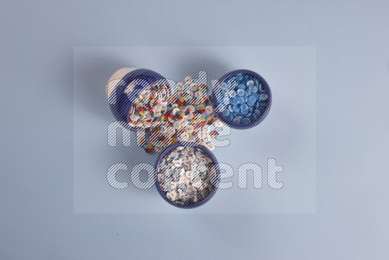 Multicolored pottery bowls full of colored buttons on blue background