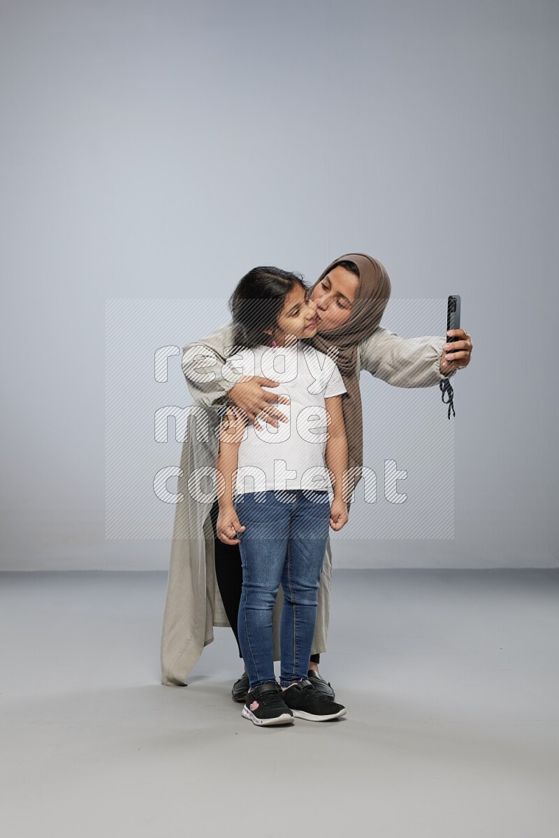 A girl standing taking selfie with her mother on gray background