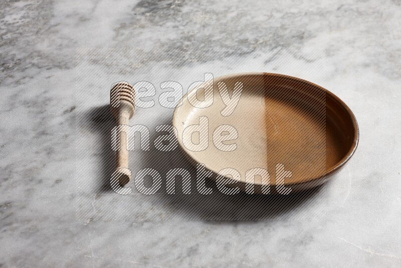Multicolored pottery oven plate with wooden honey dipper on the side on grey marble background